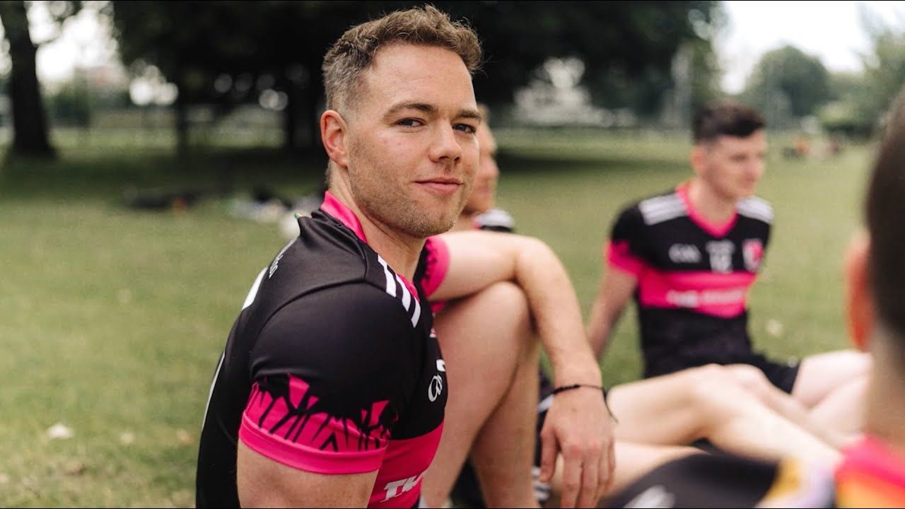 Photo of young man in sporting attire, sitting outdoors and smiling wryly to camera.