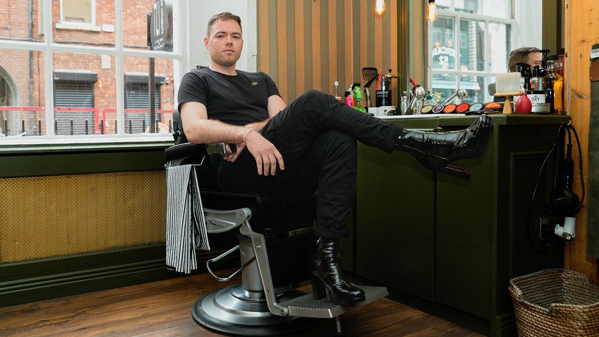 Photo of seated man on a barber chair, wearing high heels footwear.