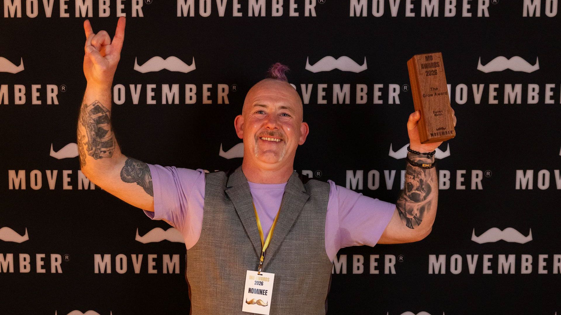 Man with mohawk hold award in front of movember media wall