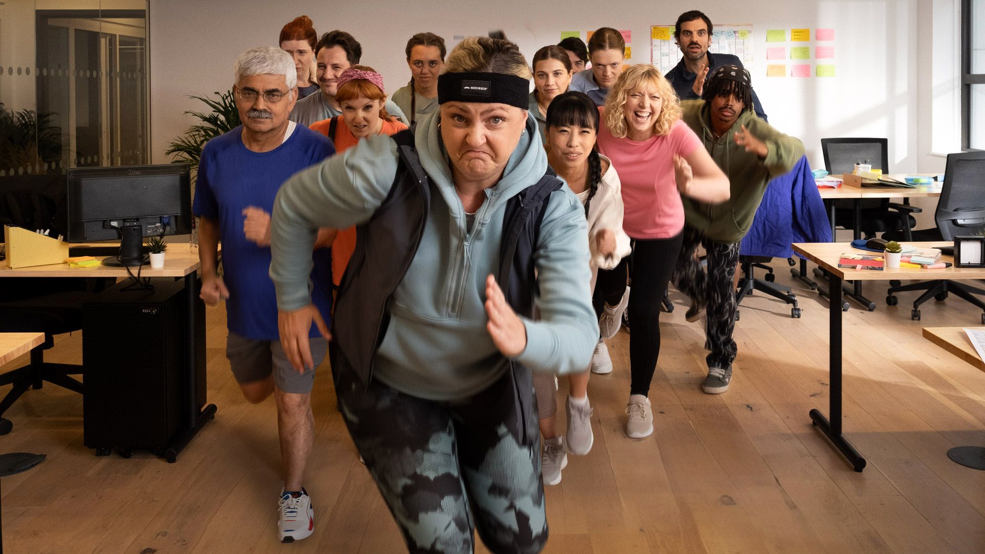 Humorous photo of people in active-wear performing a fitness routine at an office.