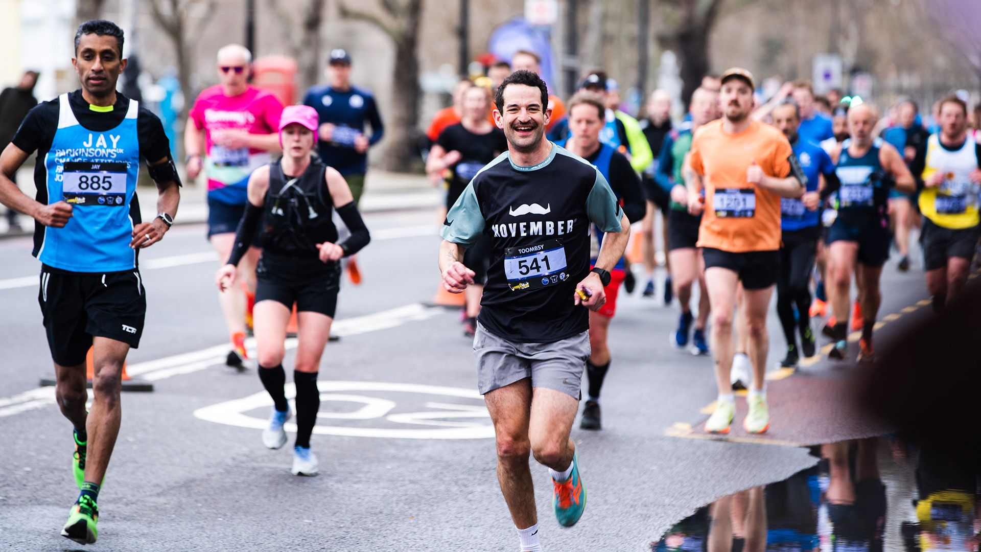 Crowd of runners in Movember-branded attire smiling to camera at a race.