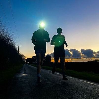 Photo of runners on a road, silhouetted against an early morning sunrise.