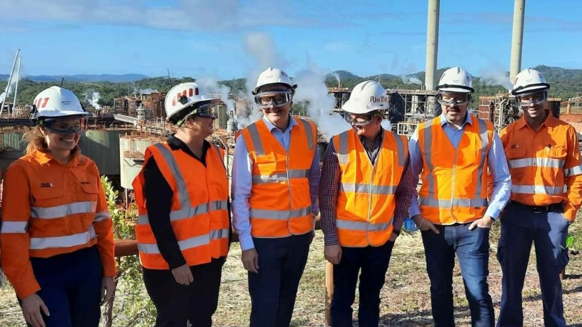 A photo of six smiling people at a mining site, wearing high vis safety 