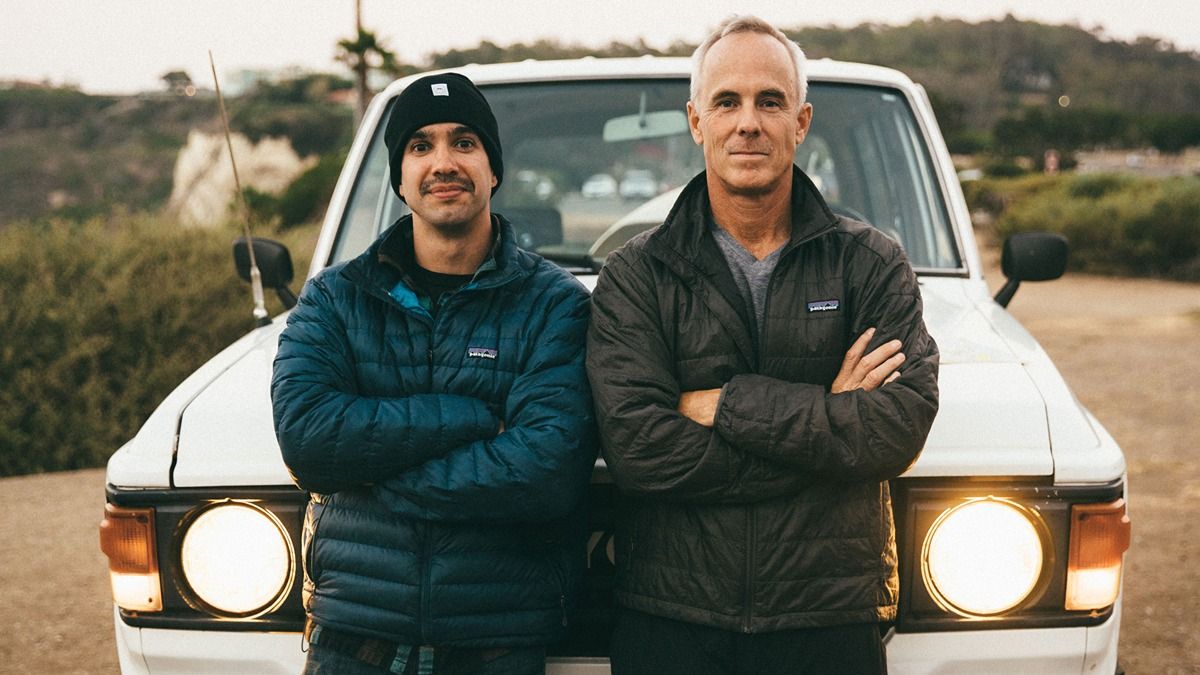 Photo of two men looking to camera while posing in front of a car.