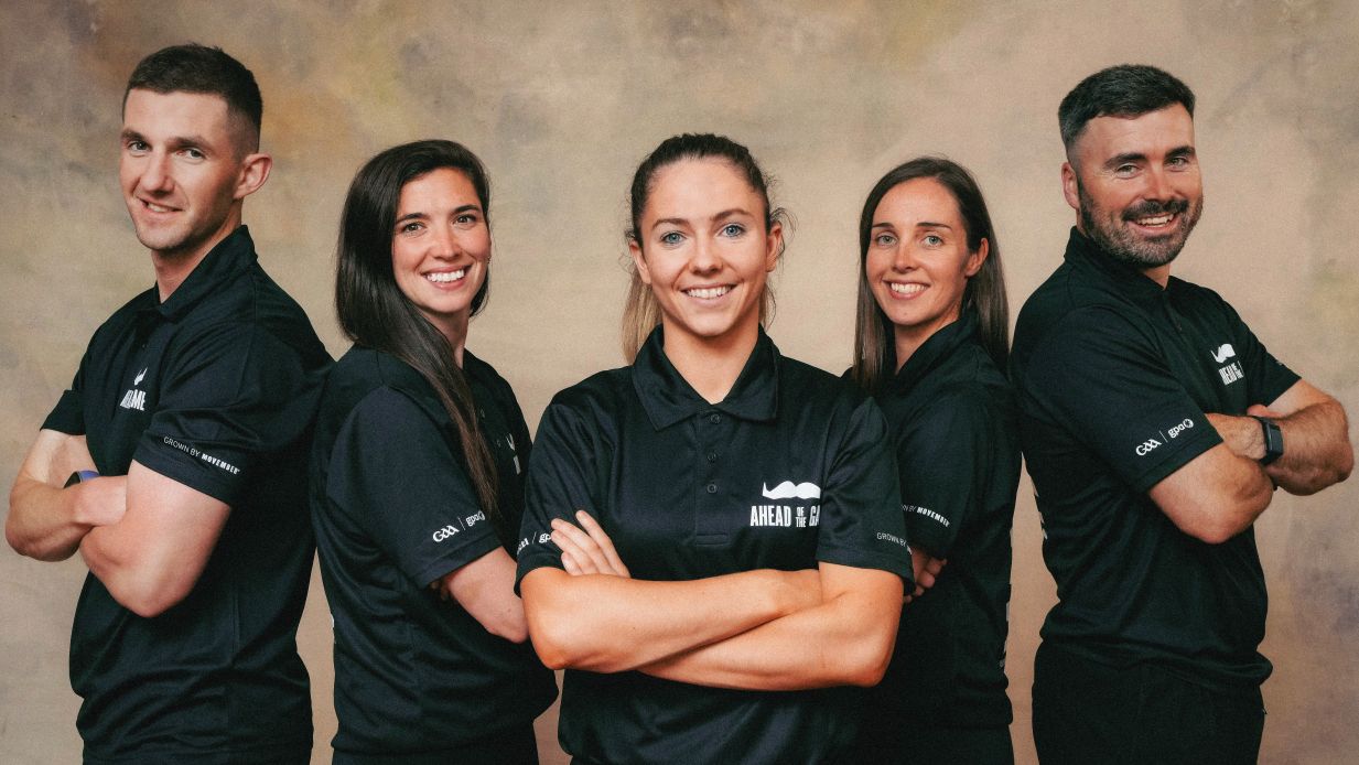 A group of Five people, three women and two men, all in black "Movember Ahead of the Game" shirts, posing with arms crossed and smiling confidently.