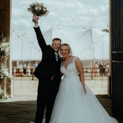 Photo of a man dressed as a groom, holding wedding flowers, and a woman dressed as a bride.