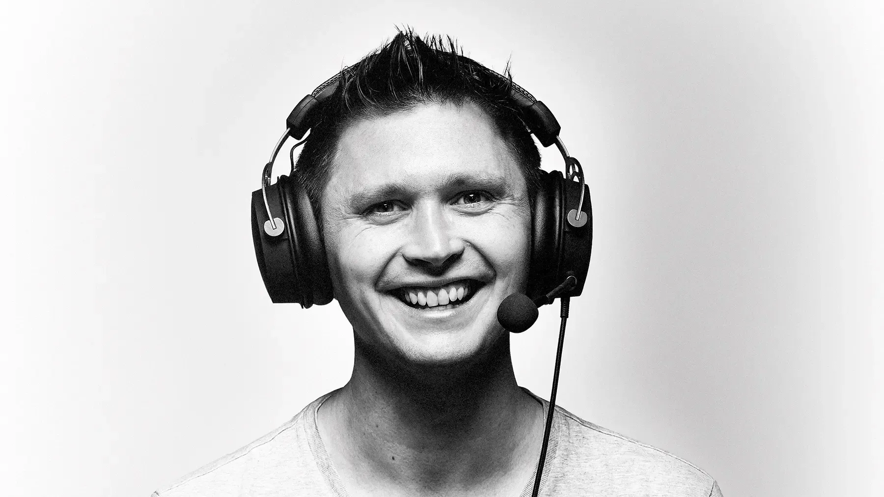 Black and white photo of man wearing gaming headset, smiling to camera.