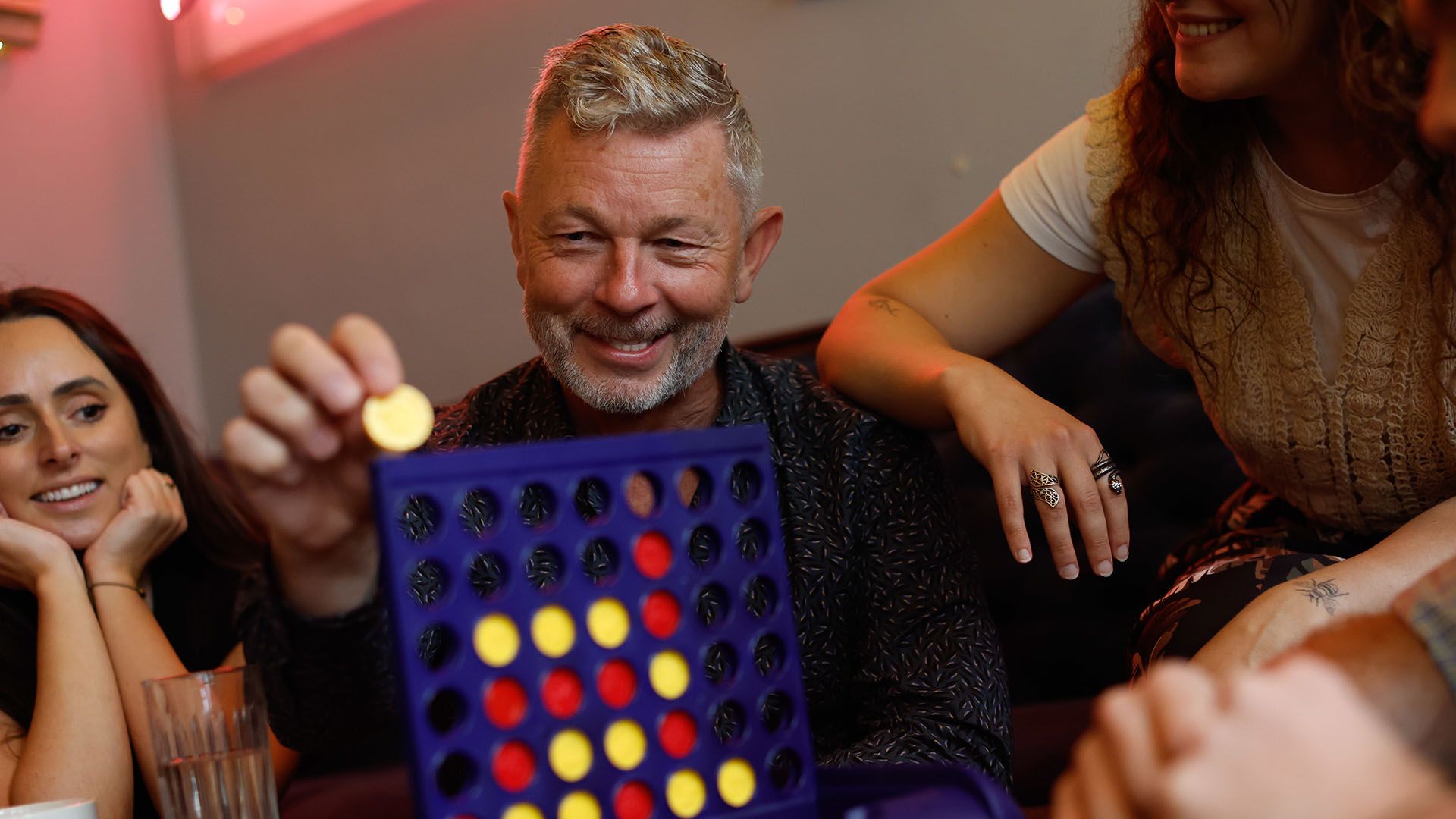 Stock photo of a man playing Connect Four with his family.