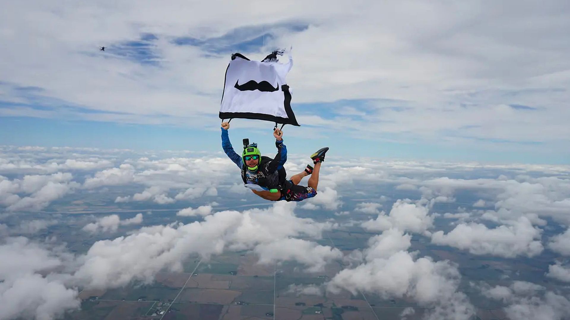 Photo of a skydiver in mid flight, holding a Movember-branded flag.