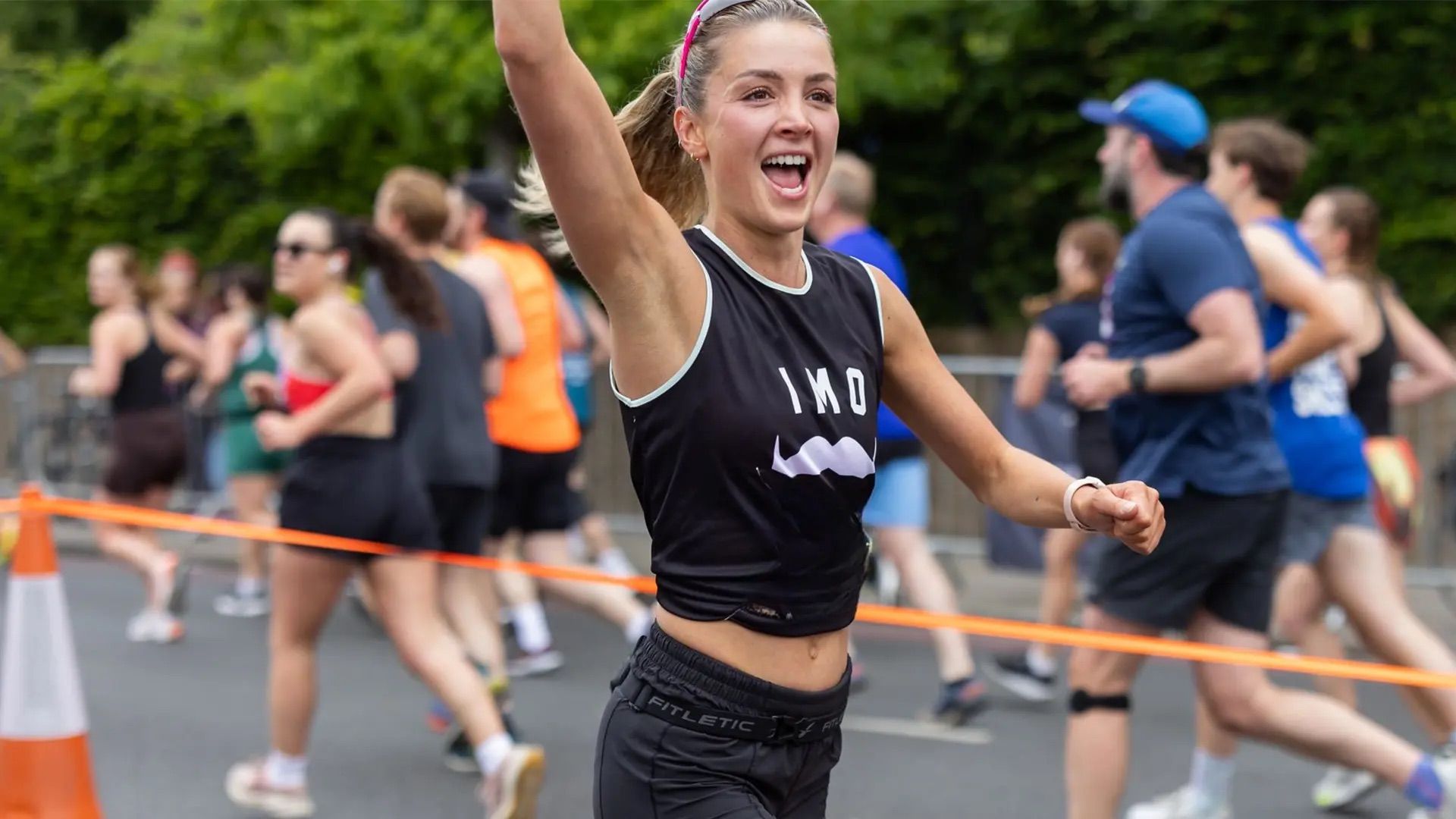 Photo of runner, wearing Movember-branded shirt, smiling and waving while running a race.