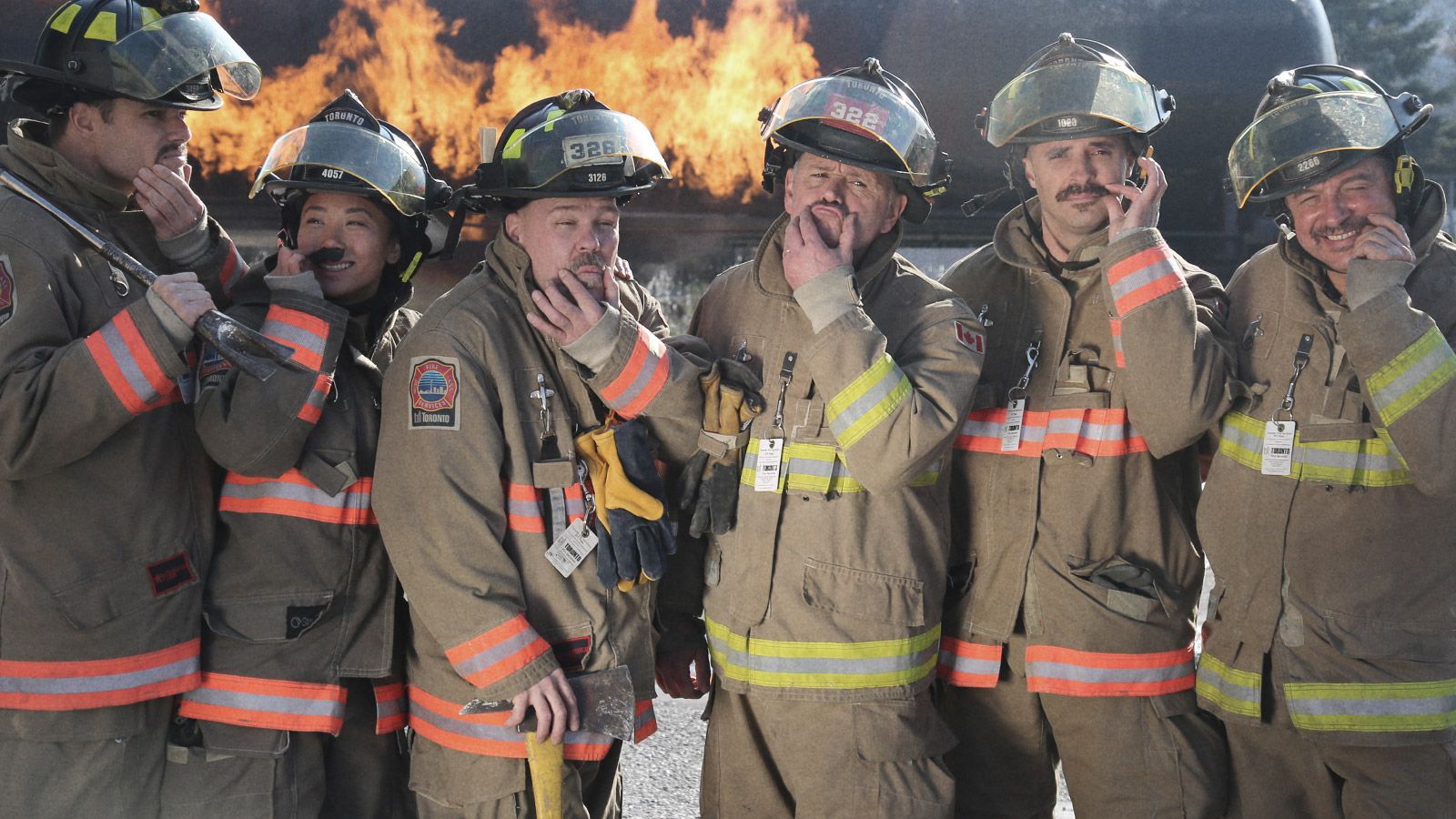 Fire fighters in uniform standing looking to camera while admiring their moustaches.