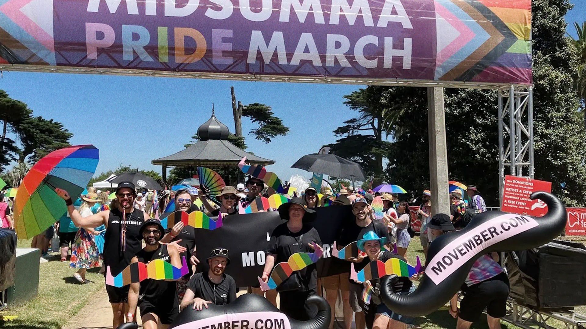 Movember employees posing with rainbow-coloured wooden moustaches at the Midsumma Pride March.