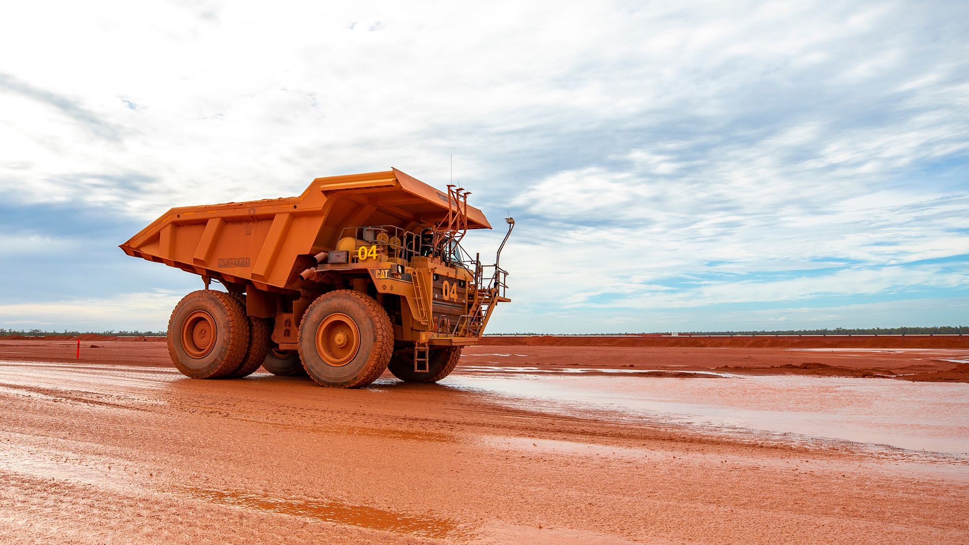 Spectacular side view photo of large mining truck. Red ground stretches all the way to the horizon.