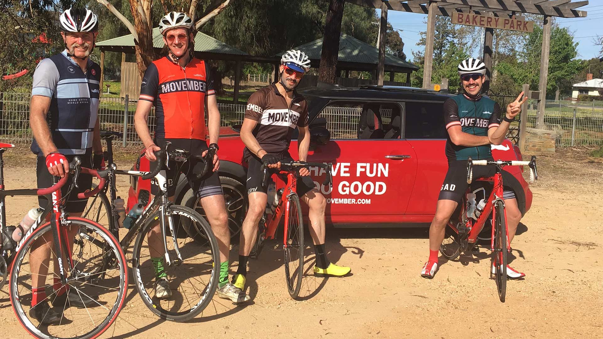 Photo of smiling off-road bike riders, wearing Movember-branded gear, smiling to camera on their bikes.